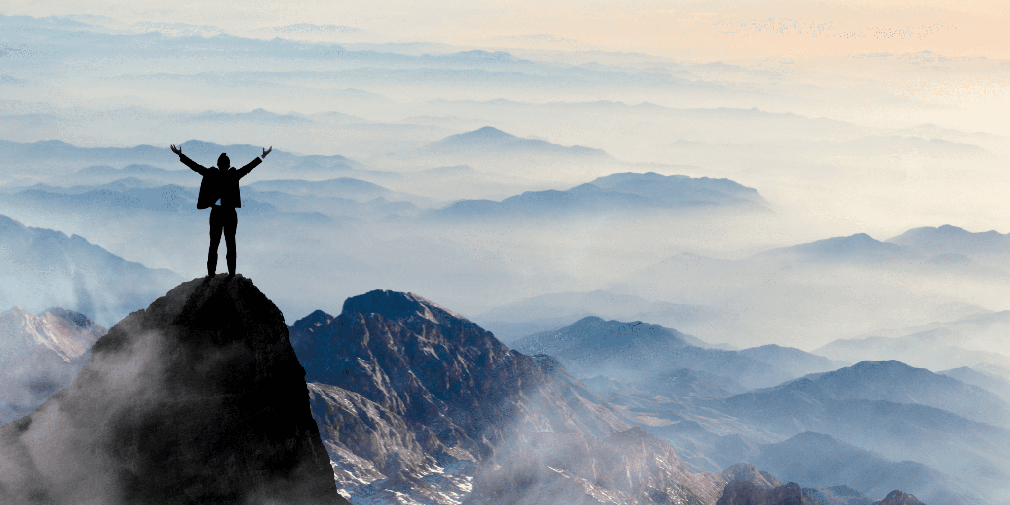 Man standing on top of a mountain overlooking the horizon, celebrating success